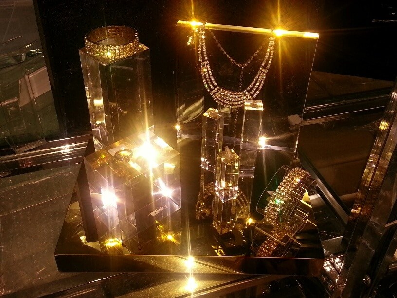 Rectangular blocks of different heights on a mirror-finish tray, with a diamante bracelet and a ring on top, lit under heavy gold light.